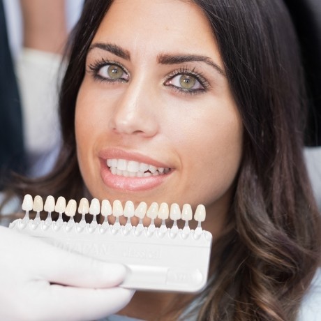 Woman smiling next to row of veneers held by cosmetic dentist in Corinth