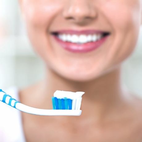 Smiling person holding a toothbrush with toothpaste on it