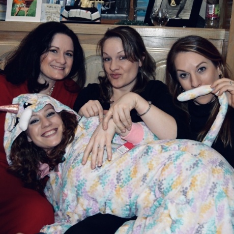 Three smiling women with fourth woman dressed in unicorn costume and laying on their laps
