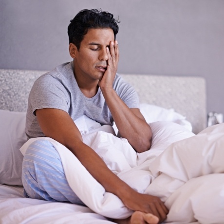 Man sitting up in bed and rubbing his eyes before sleep apnea treatment