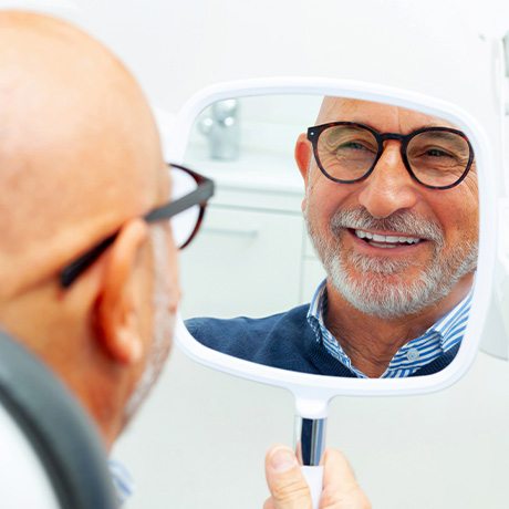 Patient with black glasses smiling at reflection in handheld mirror