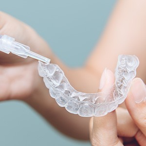 A dentist holding a teeth whitening tray and a gel-filled syringe