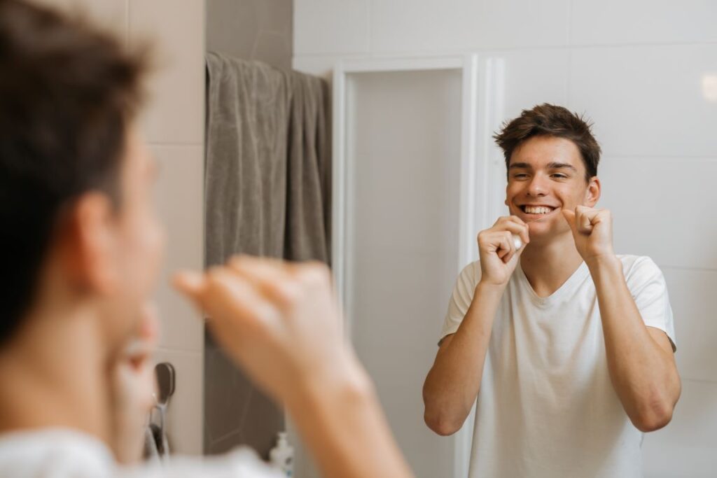 A man flossing his teeth in front of a mirror.